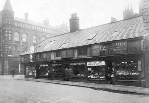 14th September 1927. On left, offices of Liverpool Victoria Insurance Offices then the junction with Albion Street. No 24 George Eastman tobacconist. No 22 Alfred Warwick violin maker. No 20 A Kirk Verity antique dealers, double fronted shop. No 18 J Easby, left window is chocolates with notice declaring fire damage to factory. Right window displays fruit. These shops were estimated to be around 200 years old. Burley Bar was situated here, the westward limit of the ancient Leeds boundary. These shops were to be demolished for improvements to what was to be called the Headrow. Text and image taken from Leodis