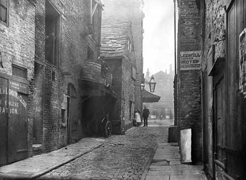 c.1887 View of the Rose and Crown Yard looking across Lands Lane to King Charles Croft. The larger of the two gas lamps is outside the Theatre Royal, the proprietor of the day was Jos. Hobson. The Rose and Crown Public House was a coaching inn, also known as 'Binks Hotel' after the landlady, Maria Binks. The Rose and Crown Yard was replaced by the Queen's arcade designed by architect, Edward Clark of London and opened in 1889. It linked Lands Lane with Briggate. From www.leodis.net