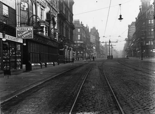 c1909. View of Briggate, looking north, and showing tram lines. Very few people are about so the photograph may have been taken very early in the morning. At the left edge is number 23 Briggate, Arthur R. Turner, Ironmonger, dealing in Oil Lamps and Stoves. Adjacent, at numbers 24, 25 and 26 is John Dyson & Sons, Watchmakers. Beyond Dyson's is the junction with Boar Lane. From www.leodis.net 