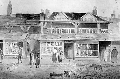 Undated View shows Middle Row. This row of shops was part of The Shambles which ran along Briggate from what would now be the junction with King Edward Street upto the entrance the County Arcade. The word Shamble comes from Seamol which was a bench where meat was displayed and sold. The Moot Hall and Middle Row behind were considered an obstruction to the throughfare of one of the city's busiest streets therefore after hundreds of years of existence, Middle Row was removed in 1825 moving to the newly opened Bazaar and Shambles between Briggate and Vicar Lane. From Leodis.net (ID: 2003122_58930606)