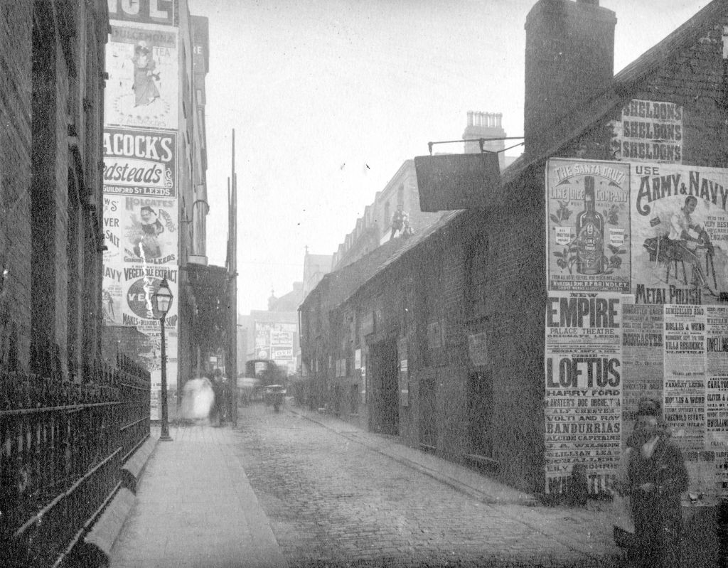 Black and white view of a narrow street with lots of advertisements on the walls of buildings.