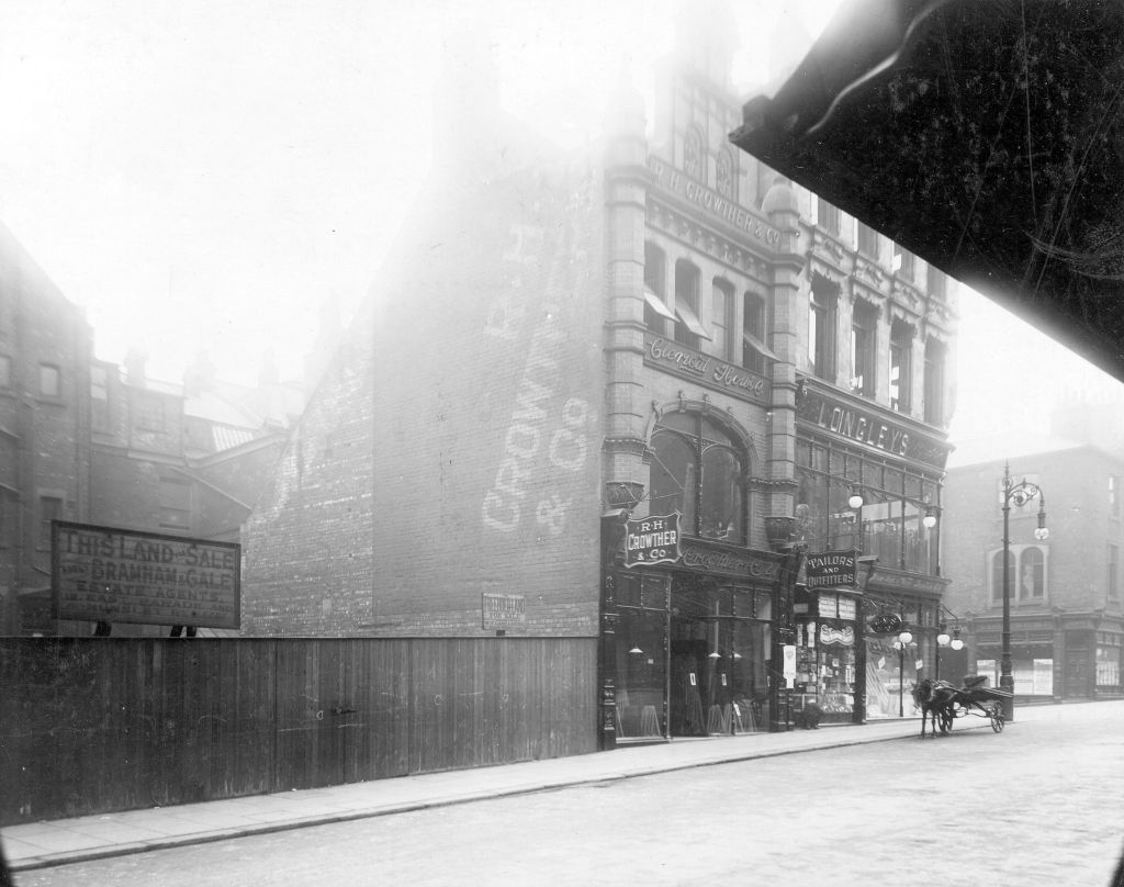 An old black and white photograph showing two shop fronts. A horse and cart stands outside one of these.