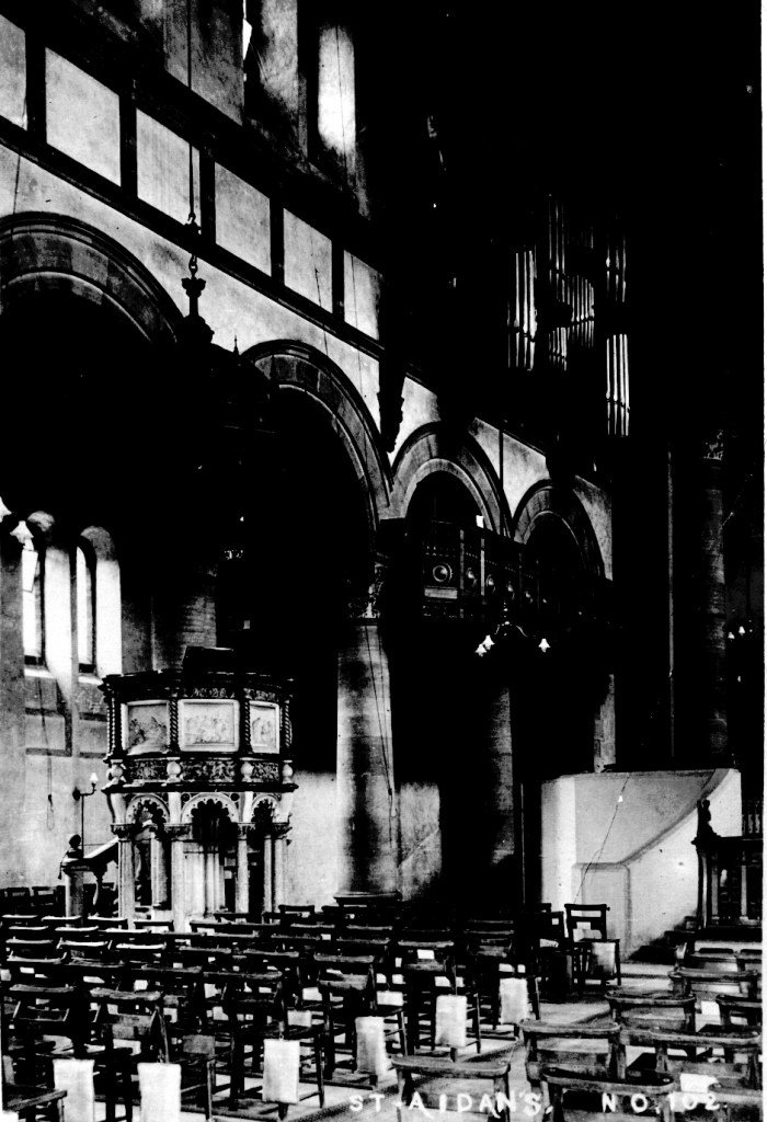 Black and white view of the inside of a church. Rows of pews are visible and a large pulpit.