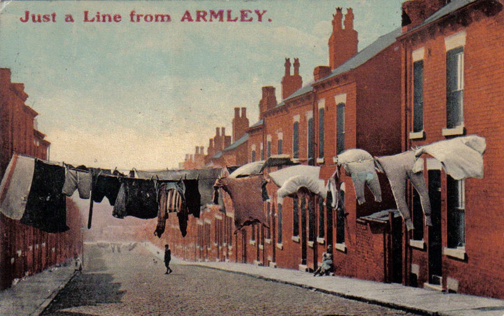 Colour postcard showing red brick terraced houses with washing lines going across the road, full of clothes.