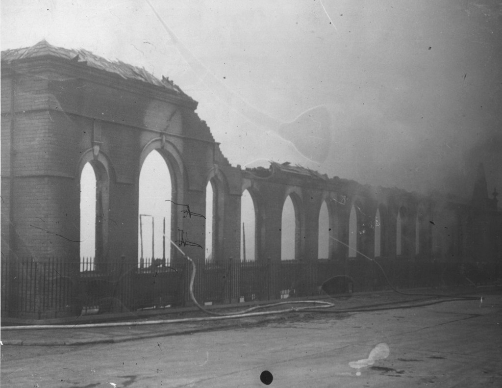 Black and white photograph showing a building with arched windows, badly damaged by fire.