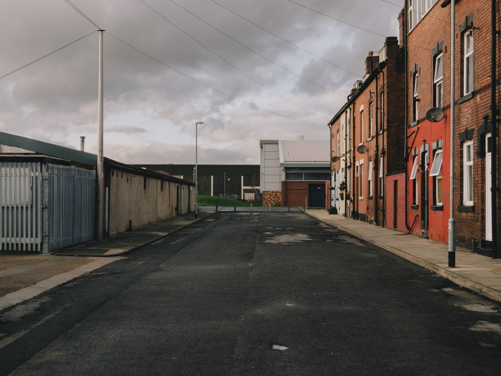 Colour photograph of a cul-de-sac in Armley with red brick terraced housing on the right side and some kind of commercial property on the left.