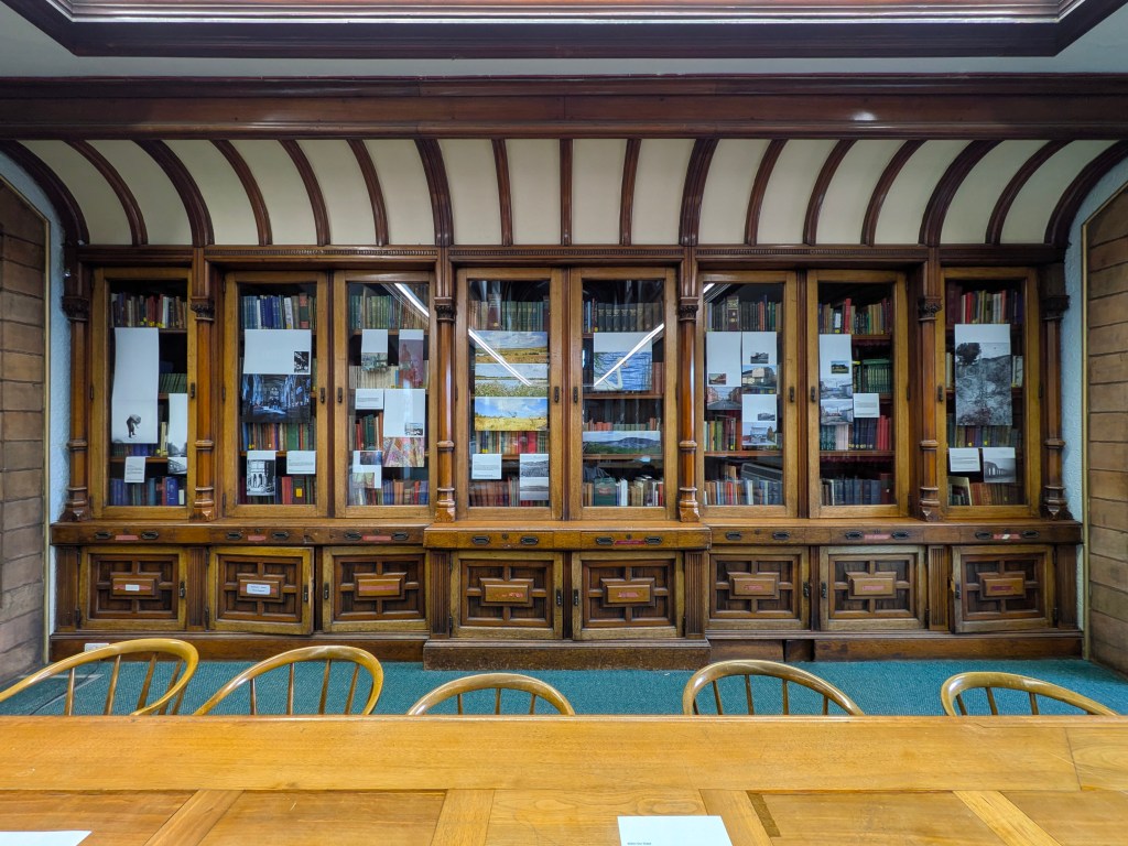 Photograph of 8 large glass cabinet filled with books and with photographs hanging from the bookshelves.