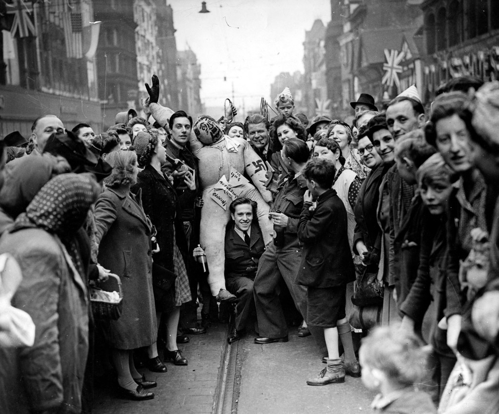 A group of soldiers and civilians stand on Briggate. One carries an effigy of Hitler on his shoulders.